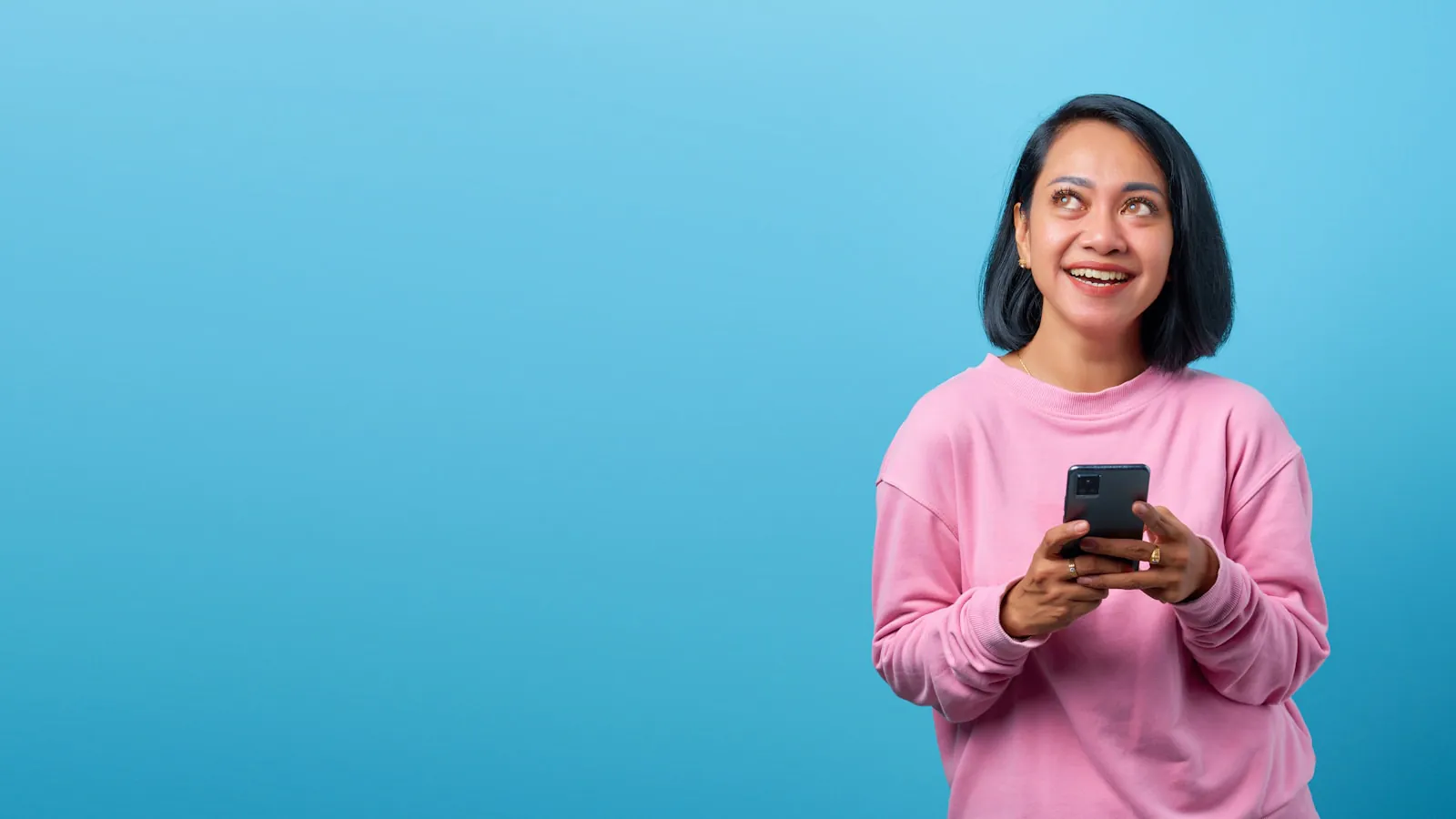 Perempuan tersenyum sambil memegang ponsel