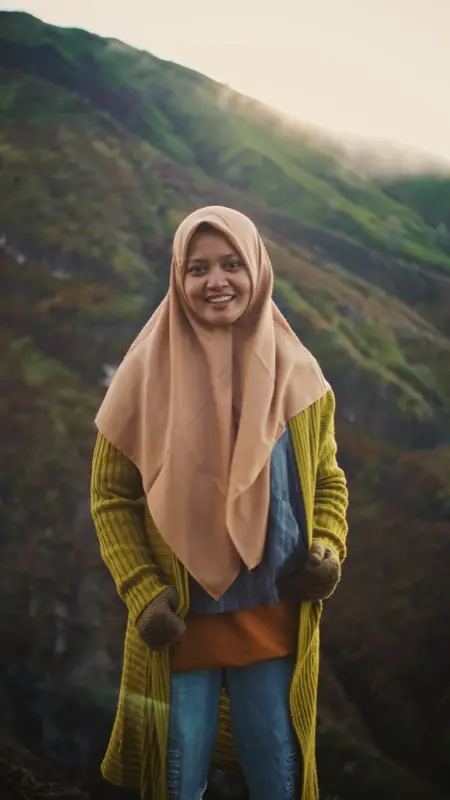 Seorang perempuan tersenyum dengan latar perbukitan