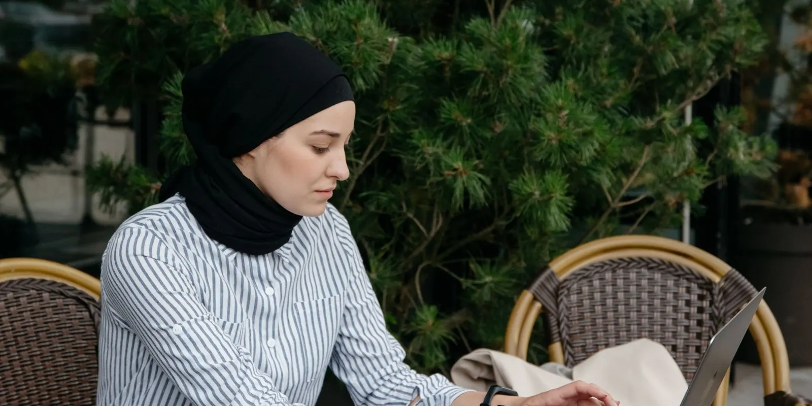 Perempuan berhijab ngetik di laptop di kafe